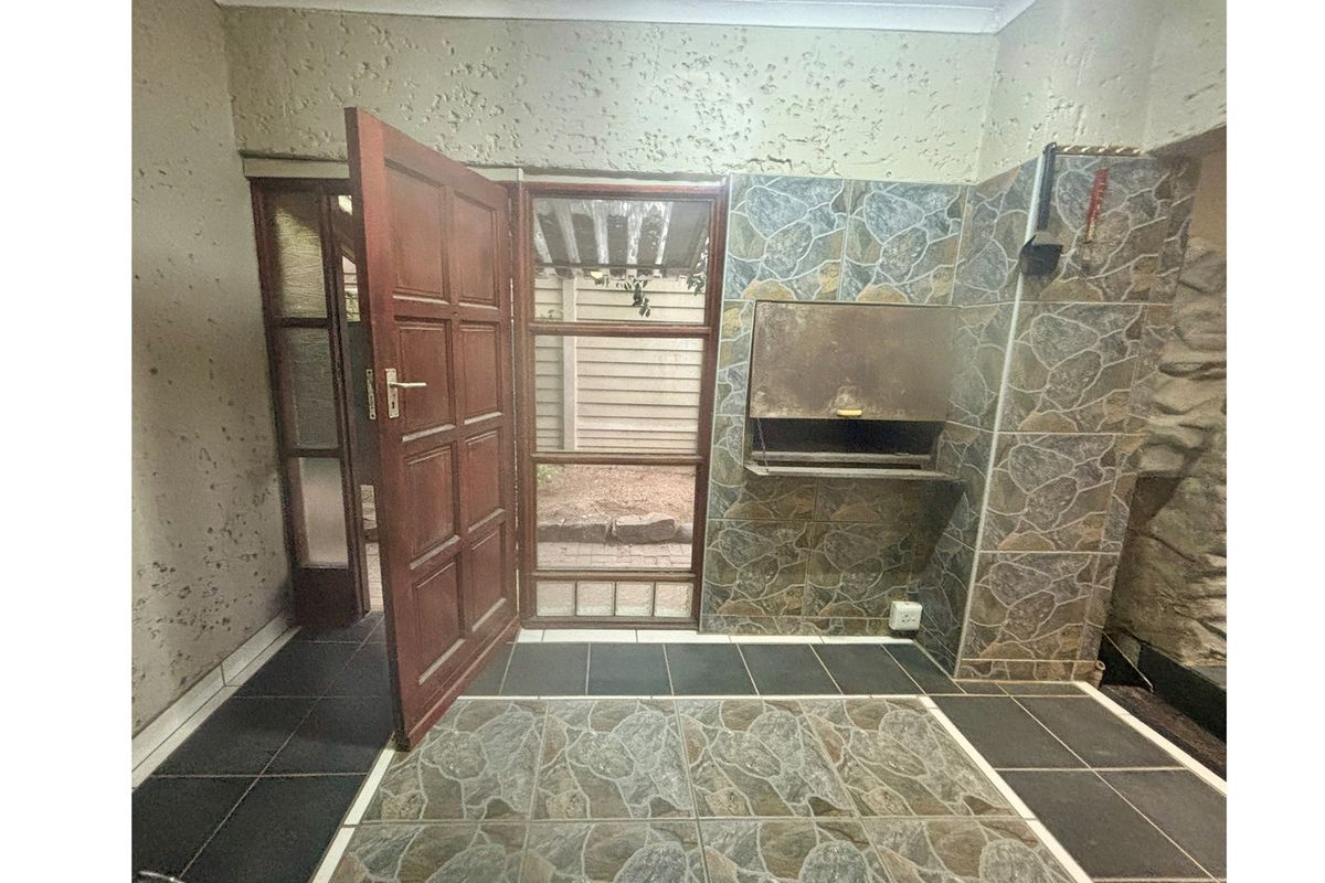 Covered patio area featuring a built-in braai, tiled flooring, and direct access to the exterior through a timber and glass door.