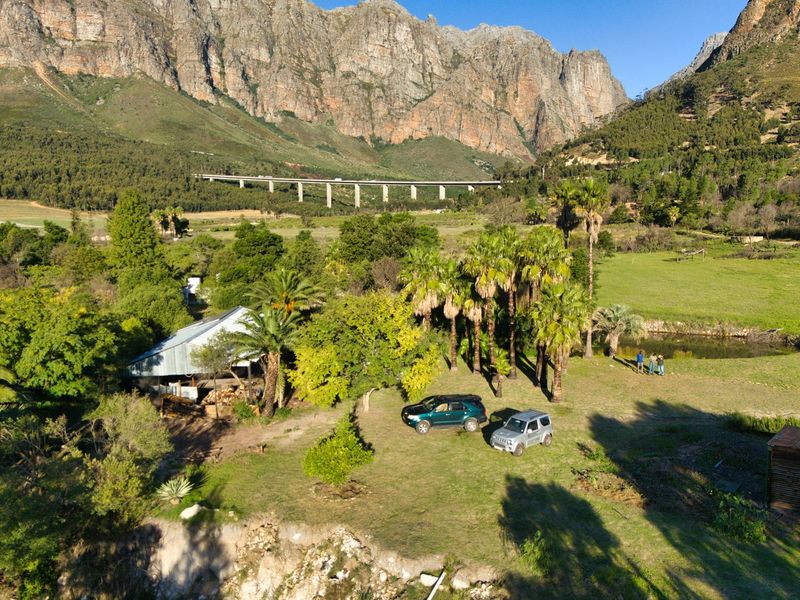Aerial view of a farm property featuring a rustic outbuilding, mature palm trees, and expansive natural grounds set against a dramatic mountain backdrop.