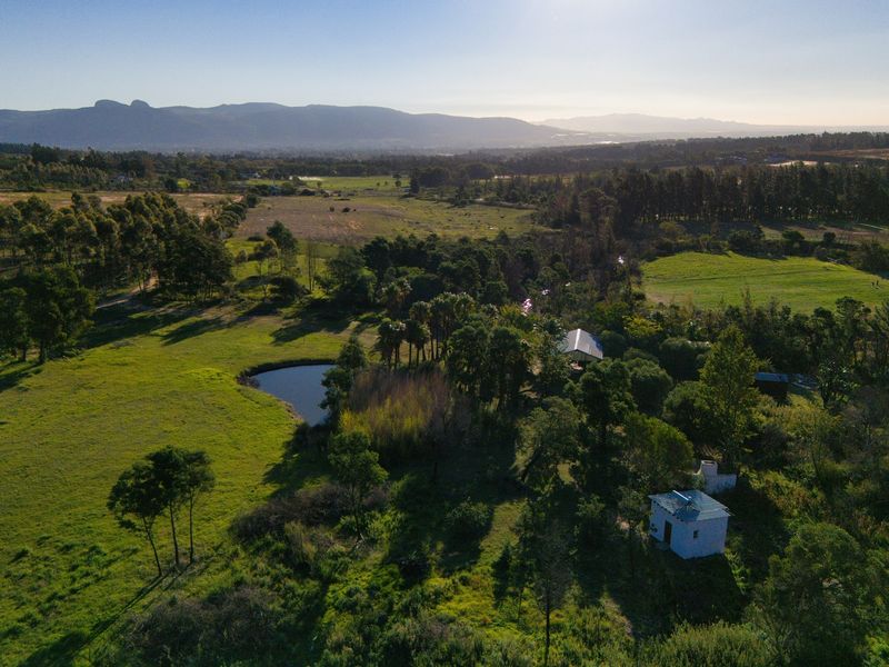 An aerial view of the farm property featuring expansive green pastures, mature trees, and a private dam set against a scenic mountain backdrop.