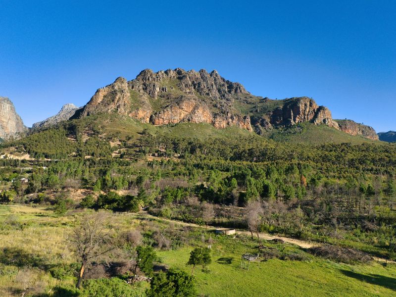 A scenic aerial view of the expansive farm landscape featuring rolling green pastures and dramatic mountain ranges in the background.
