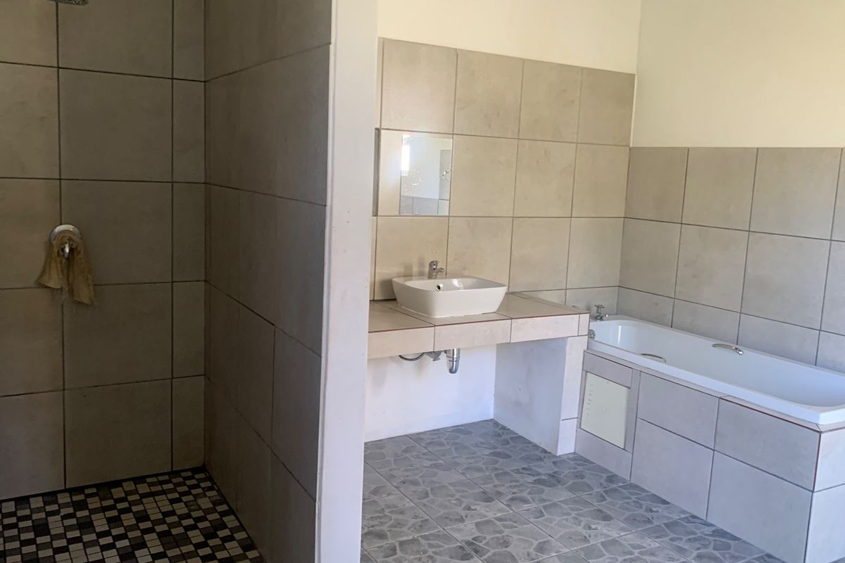 A functional bathroom featuring a walk-in shower, a built-in vanity with a vessel sink, and a standard bathtub with neutral wall tiling.
