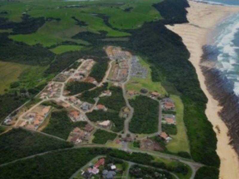An aerial view of a coastal residential estate featuring established road infrastructure and proximity to the beach and natural landscape.