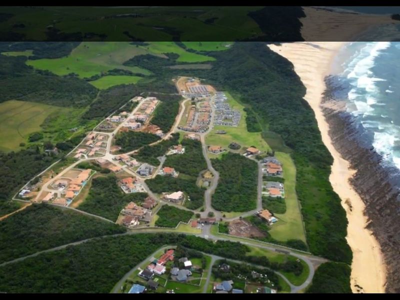 An aerial view of a coastal residential estate featuring established road infrastructure, landscaped plots, and direct proximity to the beach and ocean.
