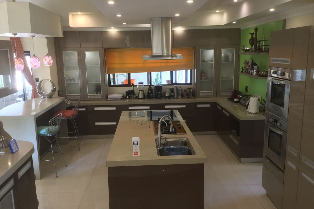 Modern kitchen featuring a central island with integrated sink and cooktop, high-gloss cabinetry, built-in double ovens, and recessed ceiling lighting.