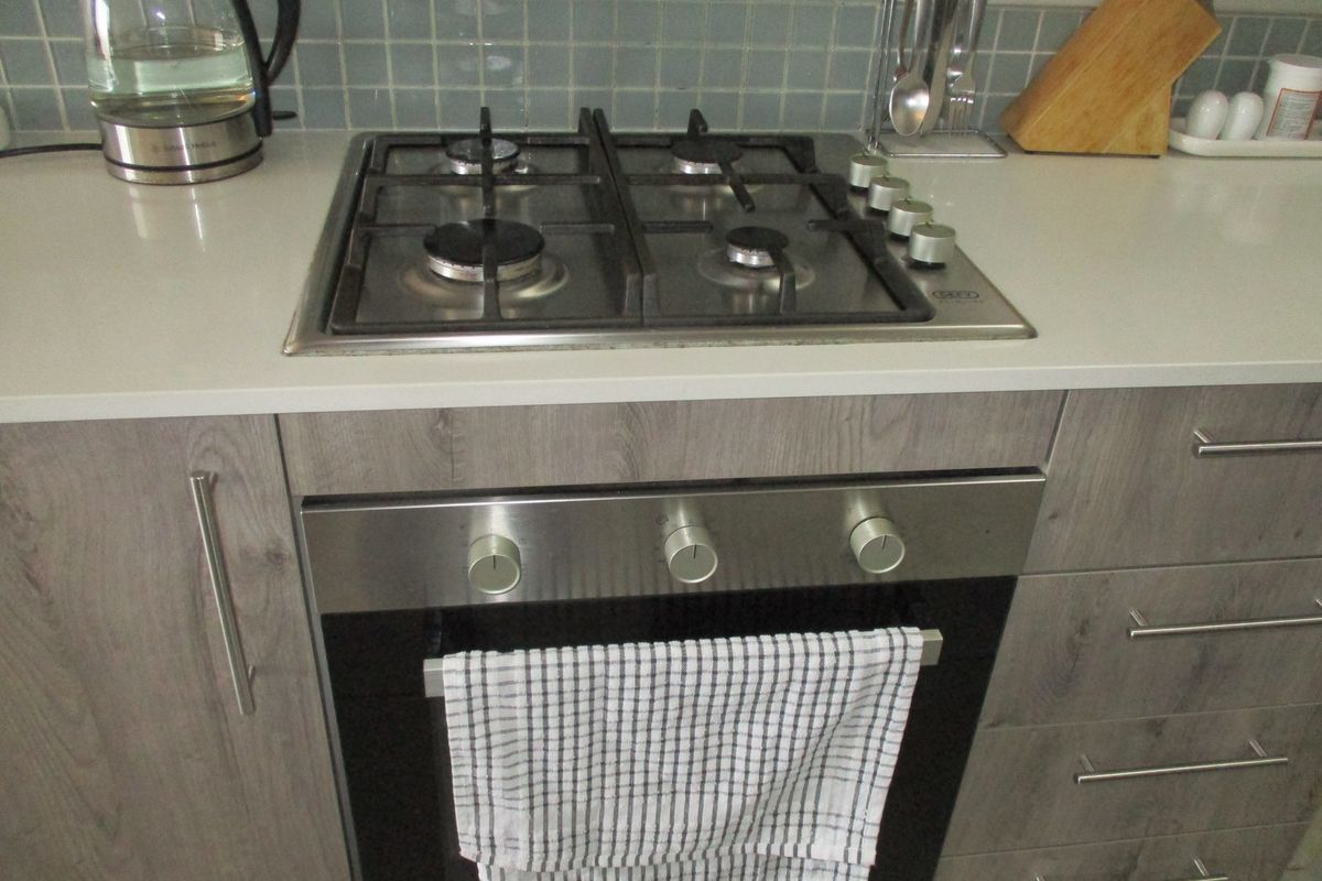 A modern kitchen featuring a built-in stainless steel gas hob and oven, complemented by grey wood-grain cabinetry and a light-toned countertop.