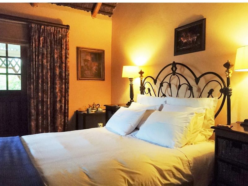 A cozy bedroom featuring a rustic thatched ceiling, warm ambient lighting, and a glass-paned door providing access to the outdoors.