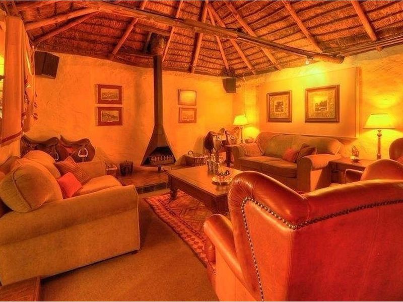 A cozy lodge-style living room featuring a traditional thatched roof, exposed timber beams, and a suspended metal fireplace.