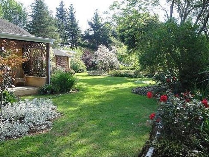 A lush, well-maintained garden area featuring a manicured lawn, mature trees, and flowering shrubs, adjacent to a covered patio structure.