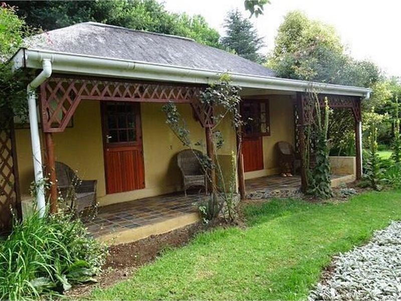 A charming lodge exterior featuring a covered patio with tiled flooring, timber lattice detailing, and stable-style doors overlooking a lush garden.