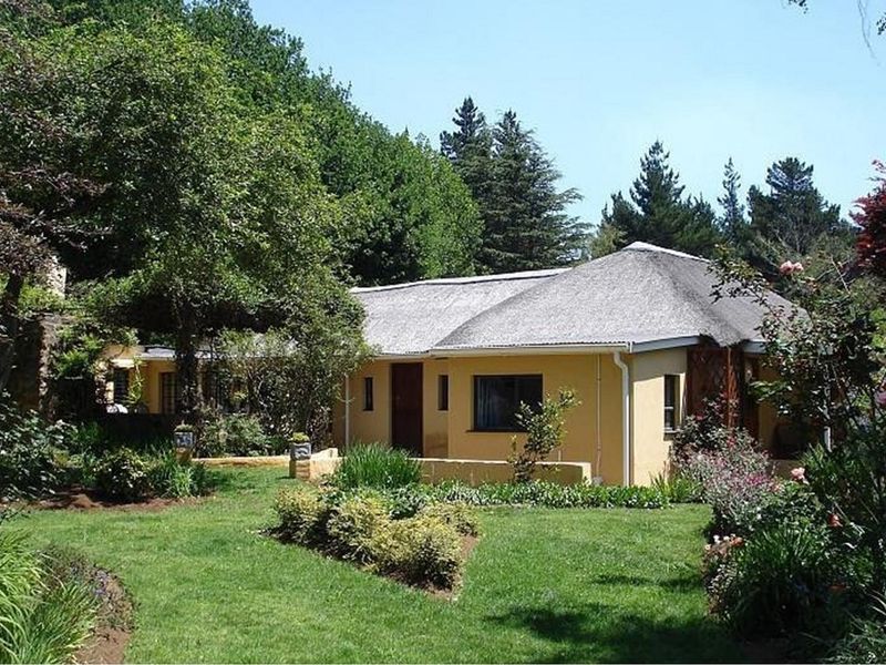 A charming lodge featuring a traditional thatched roof, set within a lush, well-maintained garden with mature trees and landscaped greenery.