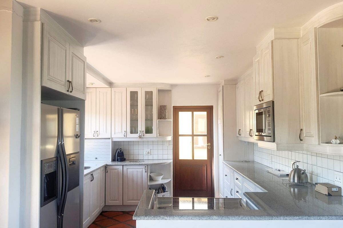 A well-maintained kitchen featuring white cabinetry, granite countertops, tiled backsplash, and a built-in microwave, leading to an exterior door.