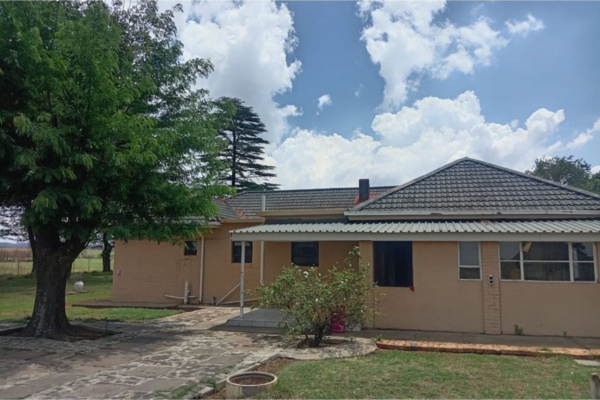 Rear view of a single-story brick farmhouse featuring a tiled roof, covered patio area, and established garden surroundings.