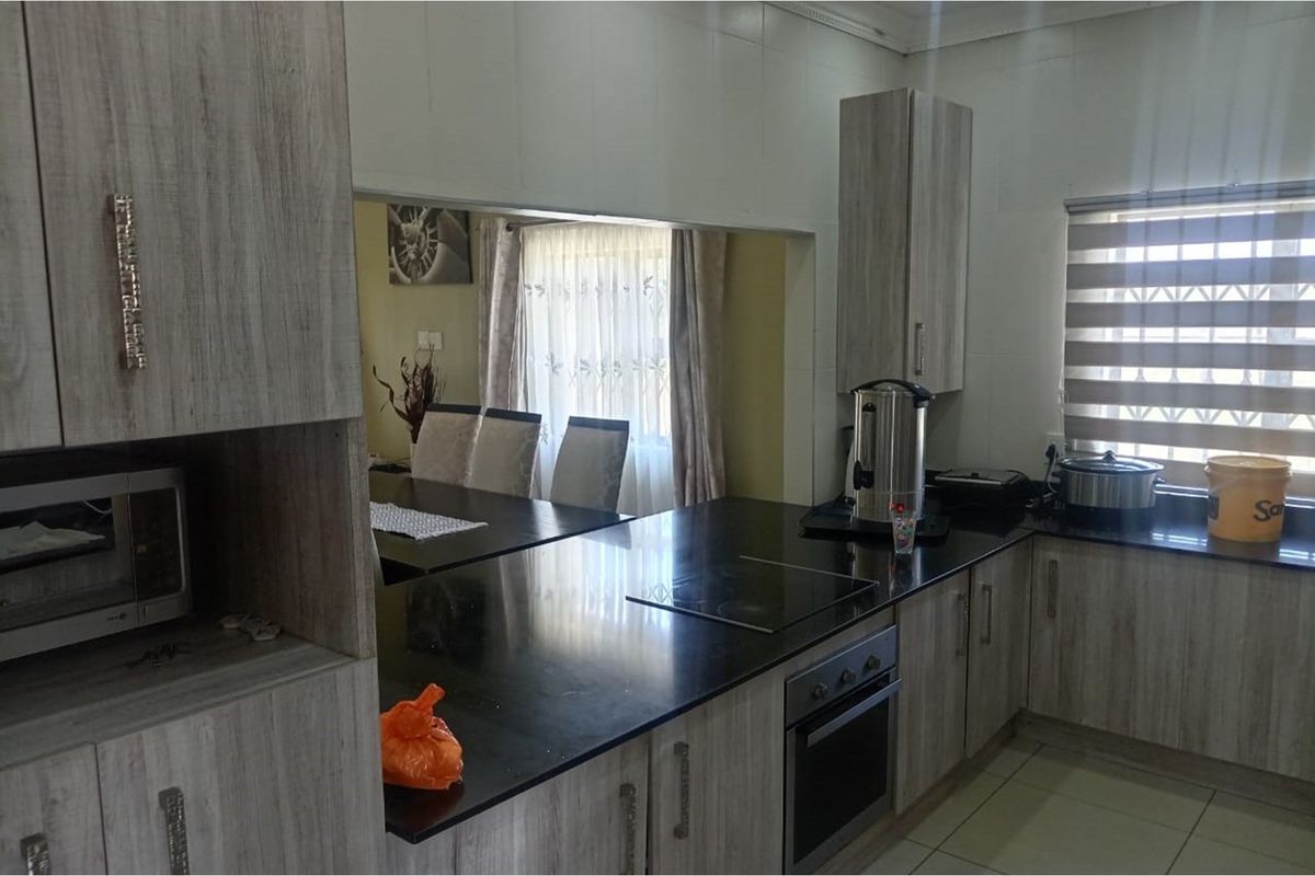 A functional kitchen featuring wood-look cabinetry, dark granite countertops, a built-in oven, and an electric hob, with a pass-through window to the dining area.