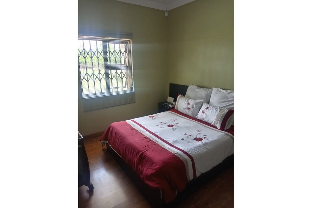 A standard bedroom featuring laminate flooring, a window with security bars, and fitted blinds.