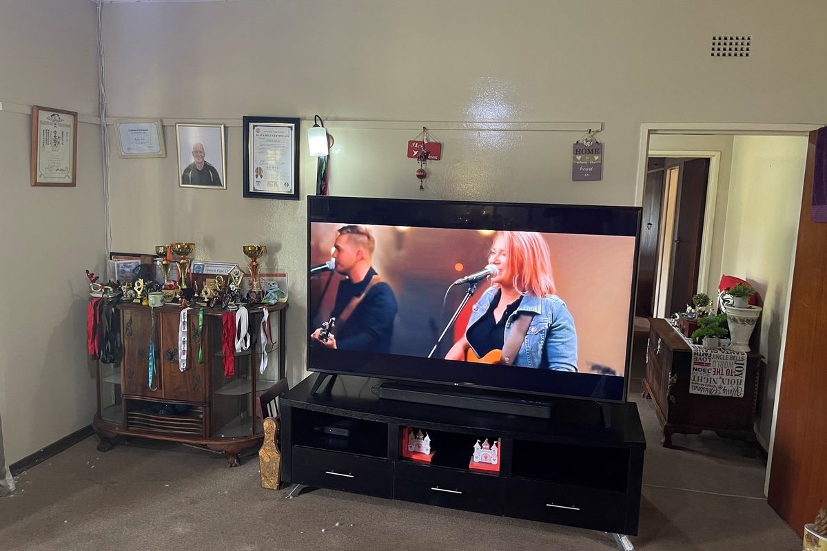 A living room space featuring a wall-mounted television area, carpeted flooring, and access to an adjacent hallway.