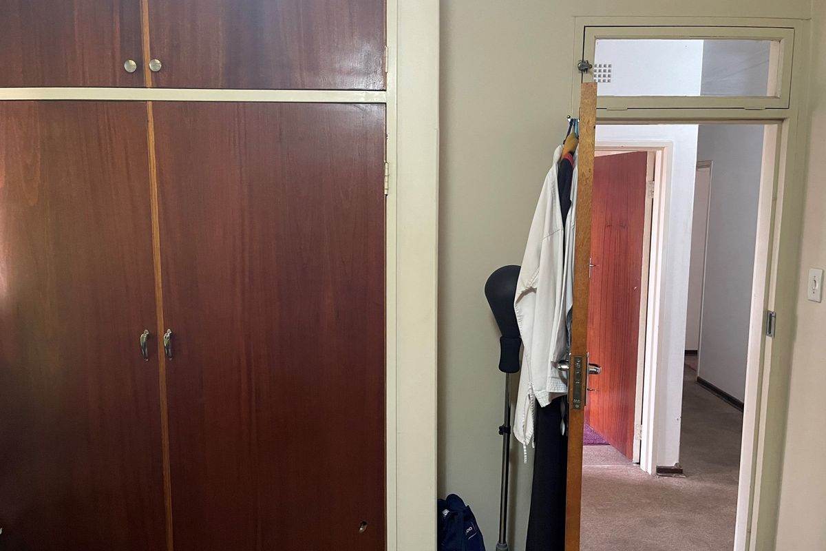 A bedroom interior featuring built-in wooden cupboards and a doorway leading to a hallway.