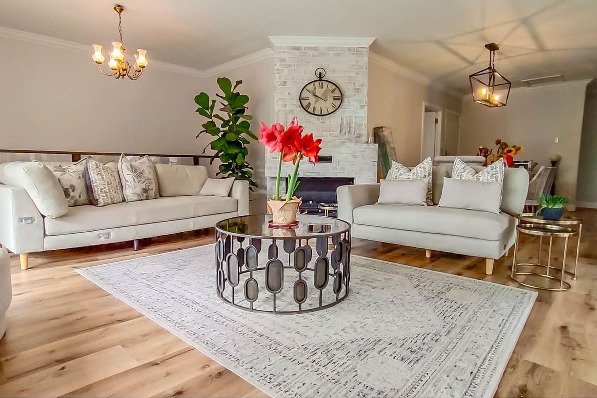 A bright and inviting living room featuring light wood-look flooring, a central brick-faced fireplace, and elegant pendant lighting.