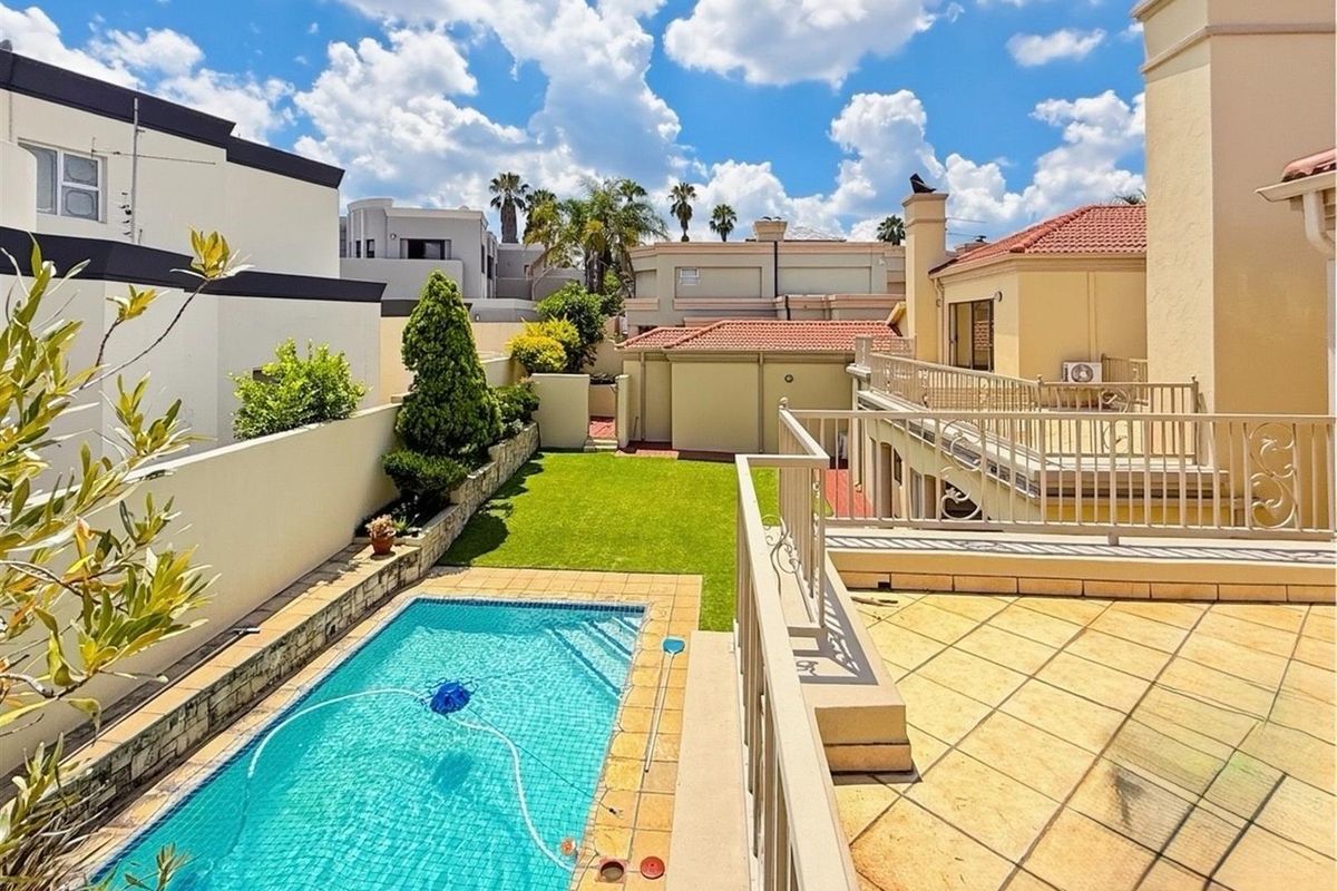 Elevated view of a private backyard featuring a swimming pool, a manicured lawn, and a spacious tiled patio area with metal railings.