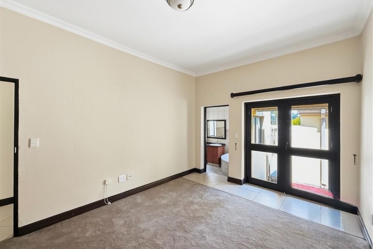 A spacious bedroom featuring neutral carpeting, crown molding, and double glass doors leading to an outdoor area, with an adjoining en-suite bathroom.