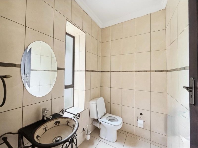 A compact bathroom featuring floor-to-ceiling beige tiling, a decorative pedestal basin, and a standard toilet.