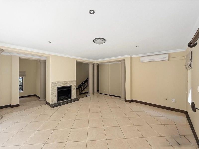 Spacious living area featuring tiled flooring, a built-in fireplace with stone cladding, decorative columns, and a wall-mounted air conditioning unit.