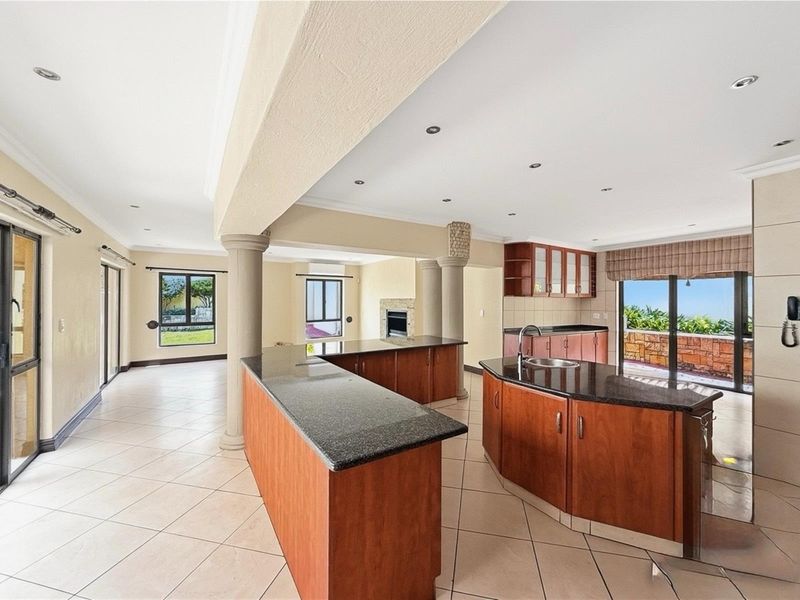 Spacious open-plan kitchen and living area featuring dark granite countertops, wooden cabinetry, tiled flooring, and direct access to an outdoor patio.