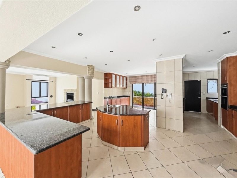Spacious open-plan kitchen featuring dark granite countertops, wooden cabinetry, a central island with sink, and integrated oven, flowing into an adjacent living area.