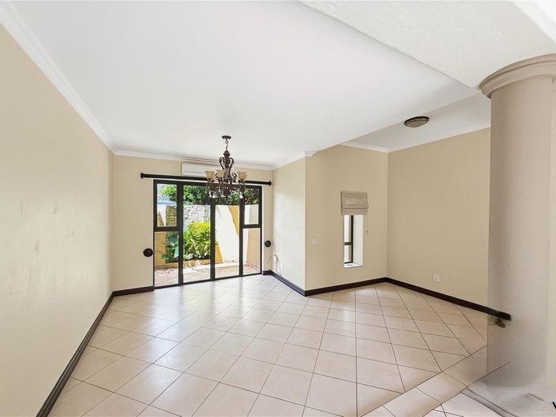 A spacious, empty living area featuring neutral tiled flooring, a decorative chandelier, and sliding glass doors providing access to an outdoor patio space.