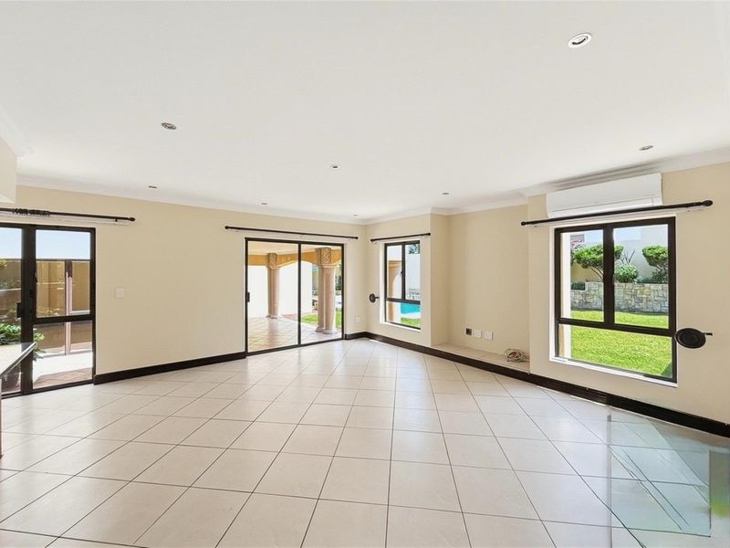 Spacious, light-filled living area featuring neutral tiled flooring, recessed downlighting, split-system air conditioning, and large windows with direct access to the outdoor patio.