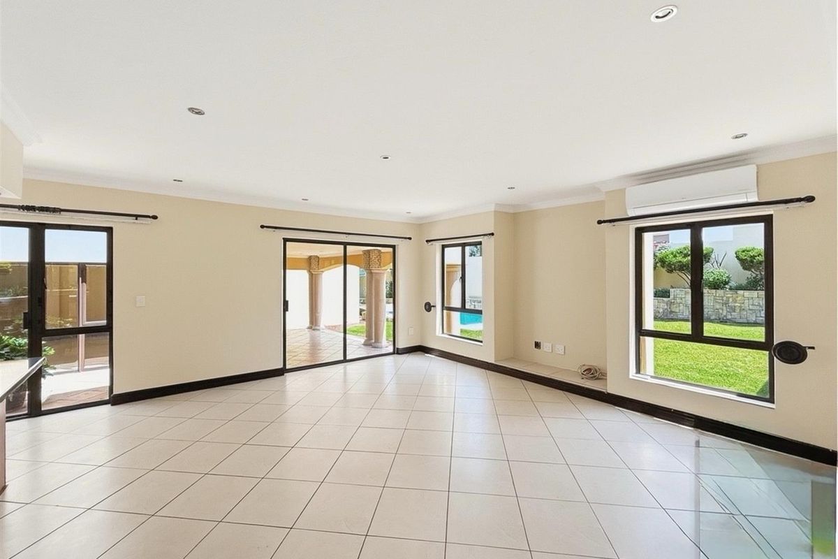Spacious, light-filled living area featuring neutral tiled flooring, recessed downlighting, split-system air conditioning, and large windows with direct access to the outdoor patio.