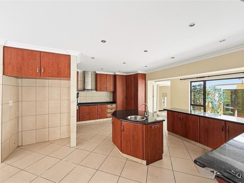 Spacious kitchen featuring dark wood cabinetry, granite countertops, a central island with a prep sink, and tiled flooring throughout.
