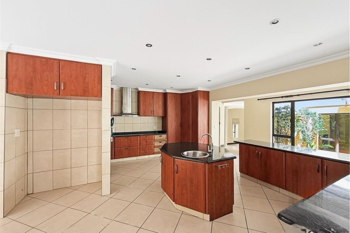 Spacious kitchen featuring dark wood cabinetry, granite countertops, a central island with a prep sink, and tiled flooring throughout.