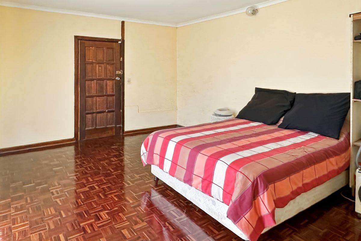 A spacious bedroom featuring traditional parquet wood flooring and a solid timber door.