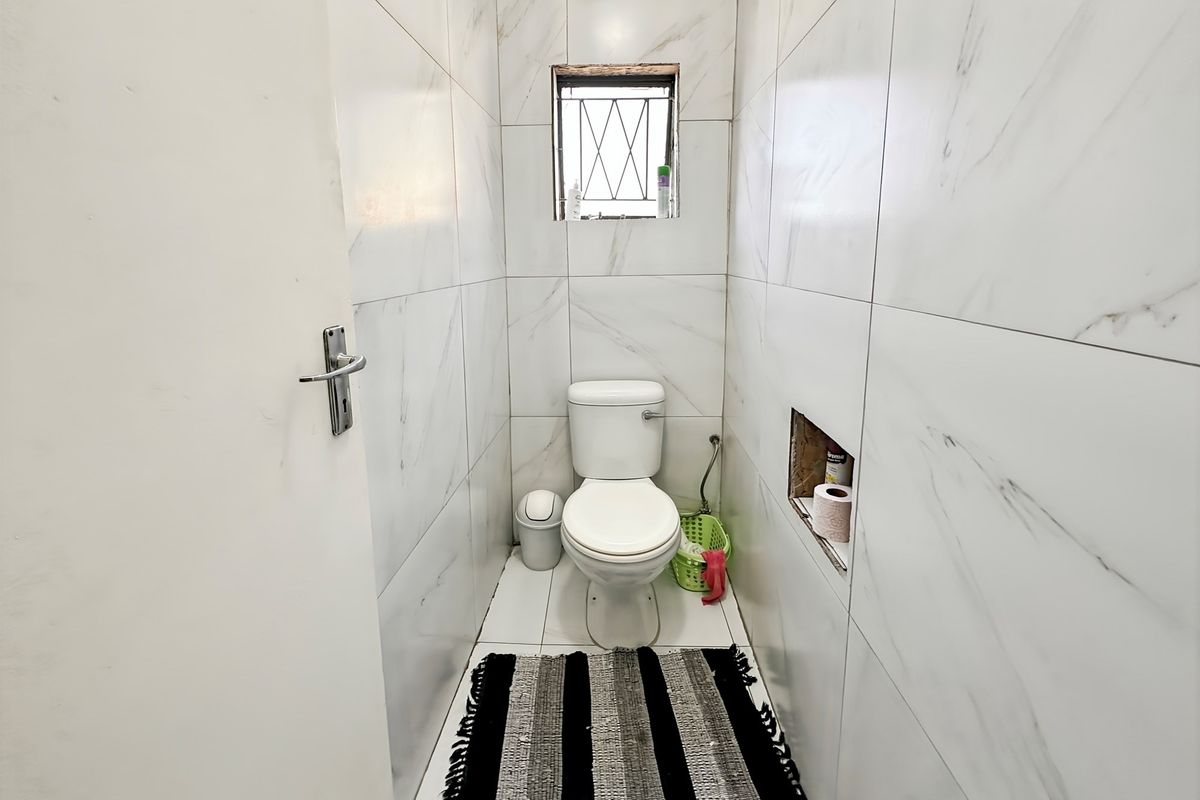 A compact guest toilet featuring floor-to-ceiling marble-look wall tiles, a standard white toilet suite, and a small high-level window.