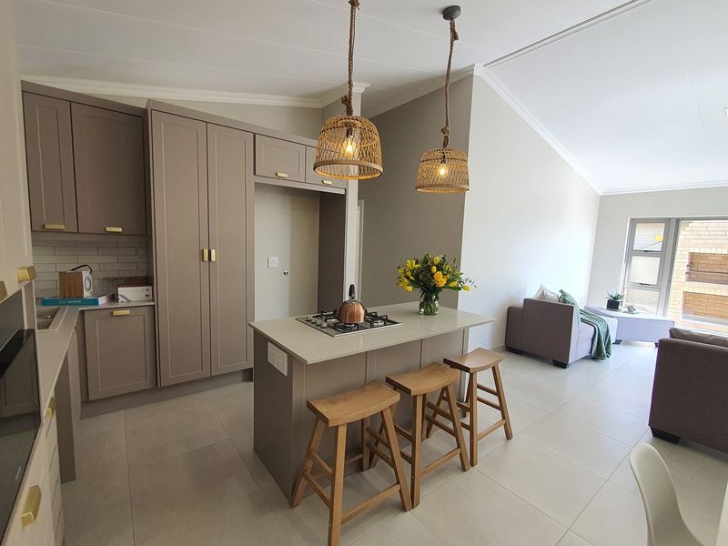 Modern open-plan kitchen featuring a central island with a built-in gas hob, sleek cabinetry, and pendant lighting, flowing seamlessly into the living area.
