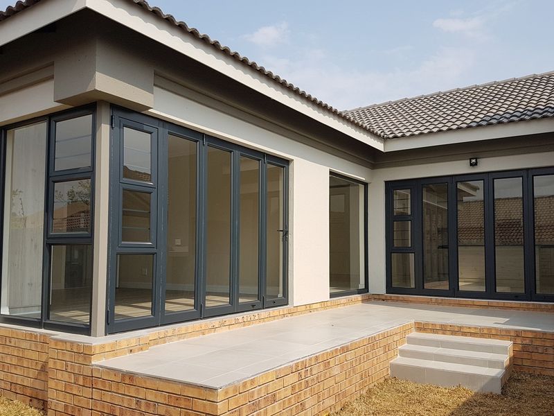A modern rear exterior view featuring a tiled patio, brick base, and large dark-framed folding glass doors providing seamless indoor-outdoor flow.