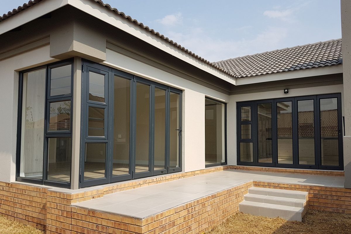 A modern rear exterior view featuring a tiled patio, brick base, and large dark-framed folding glass doors providing seamless indoor-outdoor flow.