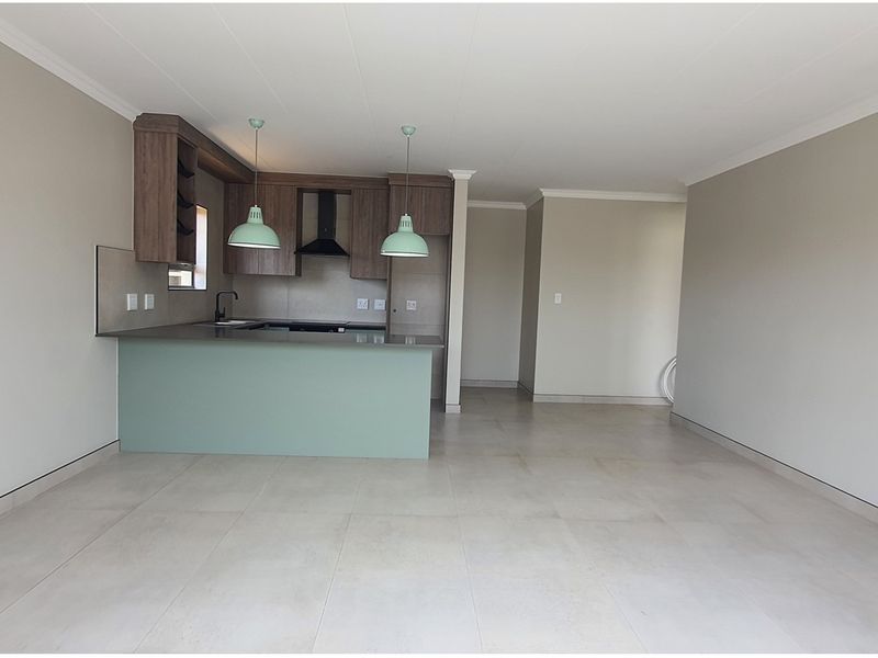An open-plan living and kitchen area featuring modern cabinetry, a breakfast counter, and neutral tiled flooring throughout.
