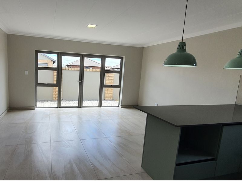 An open-plan living area featuring large glass sliding doors, tiled flooring, and a modern kitchen island with pendant lighting.