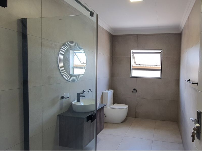 Modern bathroom featuring a glass-enclosed shower, contemporary vanity with vessel sink, and high-quality neutral floor-to-ceiling tiling.