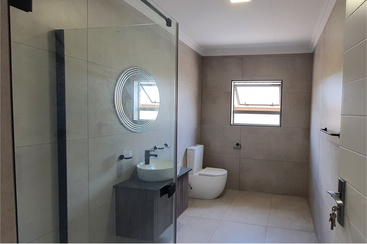 Modern bathroom featuring a glass-enclosed shower, contemporary vanity with vessel sink, and high-quality neutral floor-to-ceiling tiling.