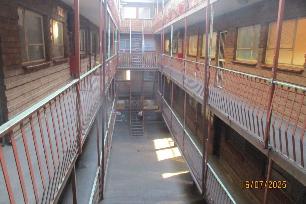 An exterior view of an apartment complex courtyard featuring multi-level walkways, metal railings, and a central staircase.