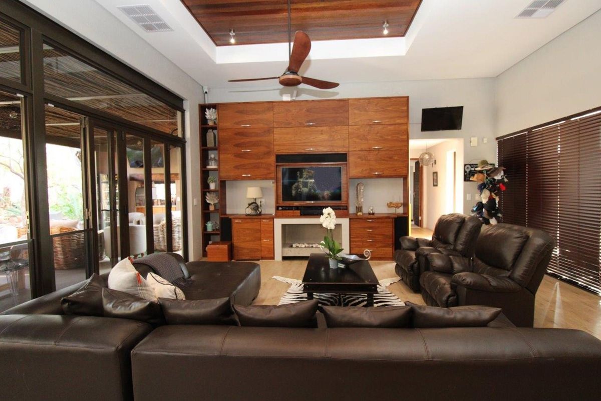Spacious living room featuring a high tray ceiling with timber inlay, built-in wooden cabinetry, and large sliding glass doors opening to the patio.