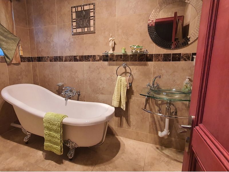 A bathroom featuring a classic clawfoot bathtub, a modern glass vessel sink with wall-mounted fixtures, and full-height decorative wall tiling.