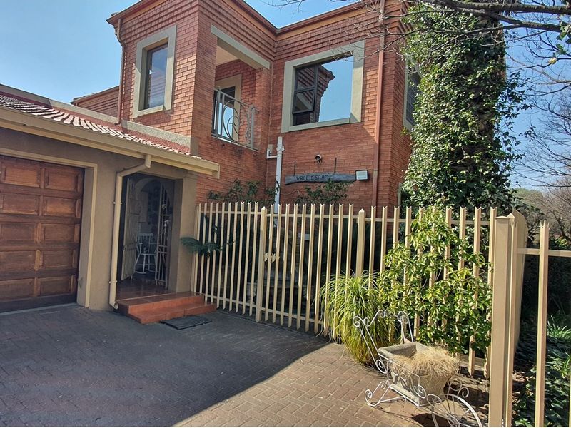 Front elevation of a double-story face-brick house featuring a paved driveway, single garage, and secure perimeter fencing.