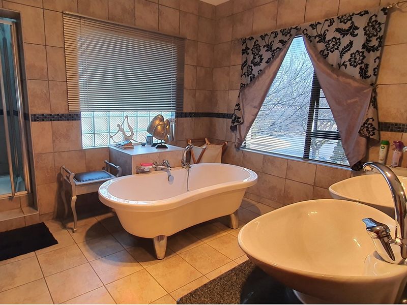 A spacious bathroom featuring a freestanding bathtub, dual vanity basins, a glass-enclosed shower, and neutral floor-to-ceiling wall tiling.