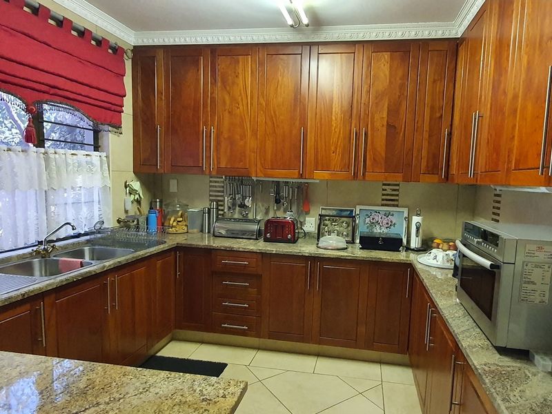 A functional kitchen featuring warm-toned wooden cabinetry, granite countertops, a double-basin sink, and built-in oven, offering ample storage and workspace.