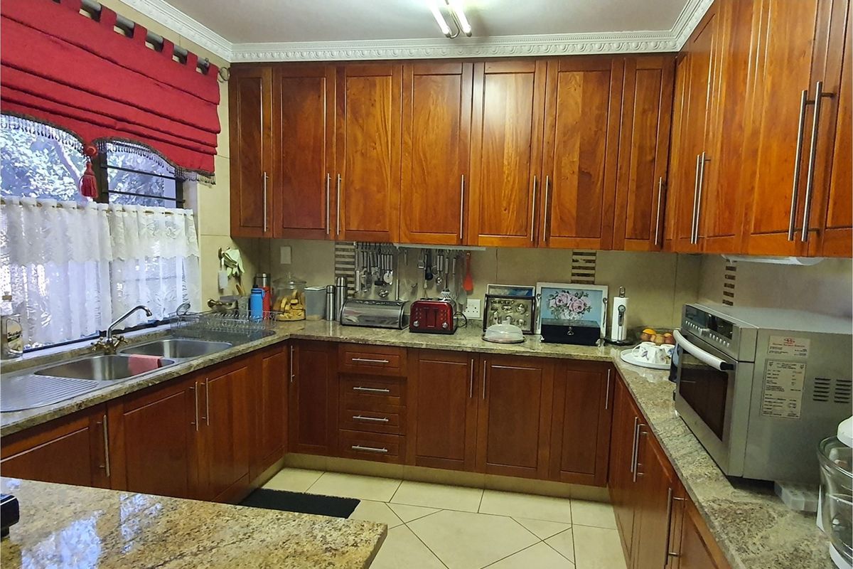 A functional kitchen featuring warm-toned wooden cabinetry, granite countertops, a double-basin sink, and built-in oven, offering ample storage and workspace.