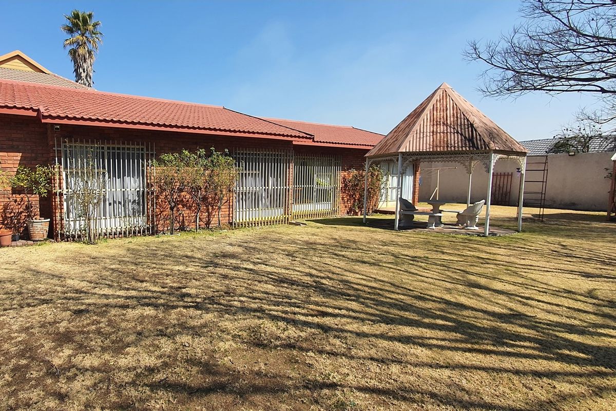 Rear view of the property featuring a brick facade with security bars and a detached gazebo set within a spacious garden area.