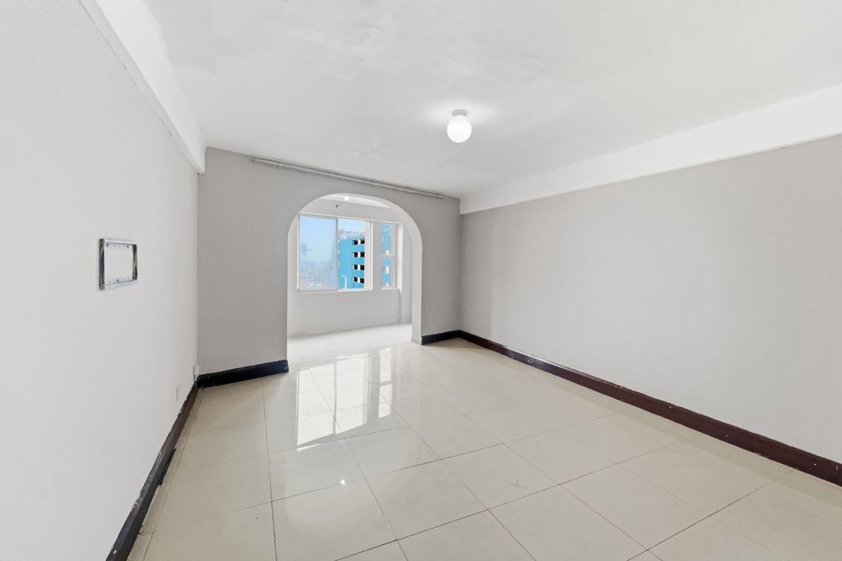 A bright, empty living room featuring neutral tiled flooring, an arched transition to an adjacent space, and simple ceiling lighting.